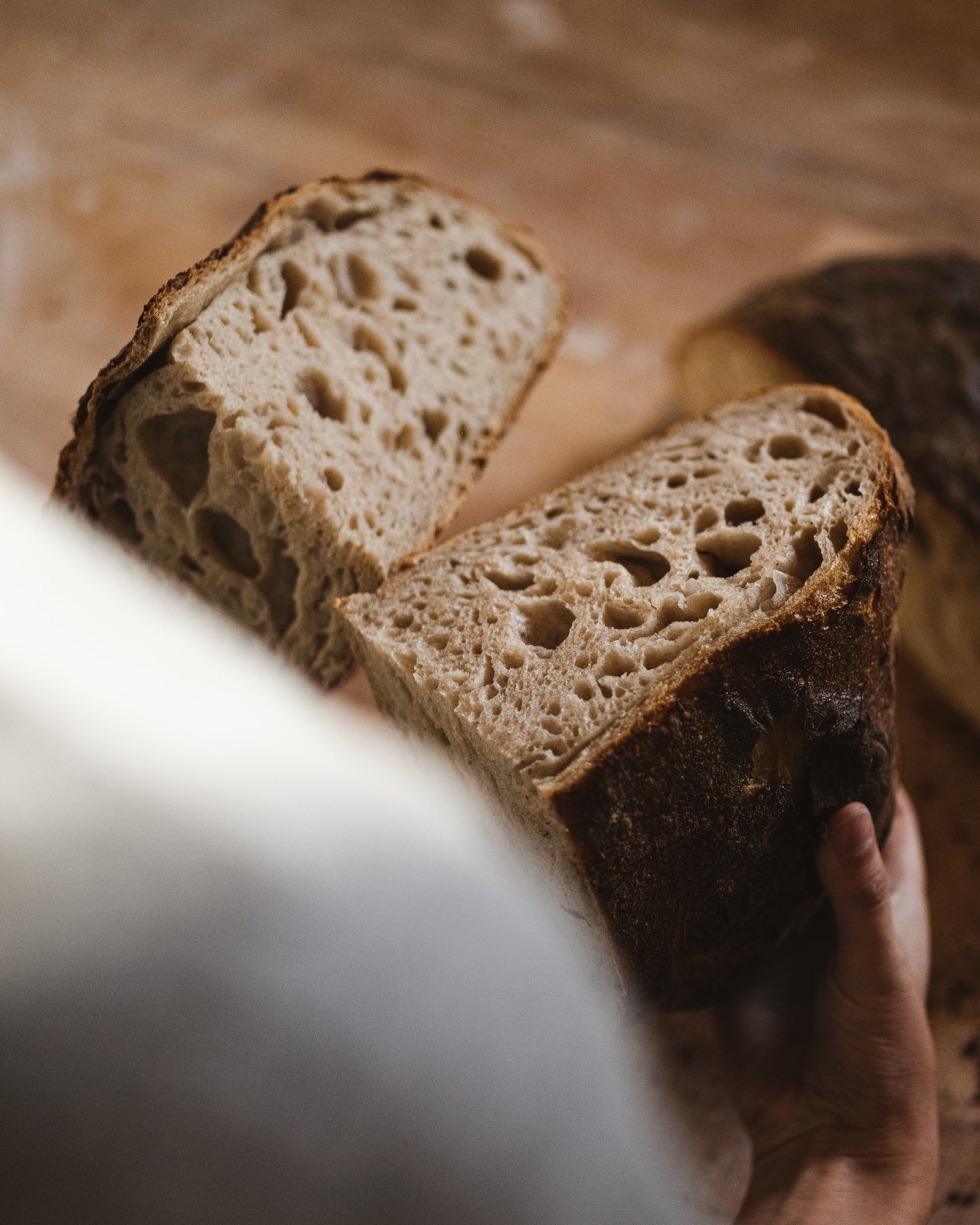 Eine Person h&auml;lt ein aufgeschnittenes Brot mit einer dicken Kruste und einer luftigen, porigen Krume. Die Schnittfl&auml;che zeigt gro&szlig;e L&ouml;cher.